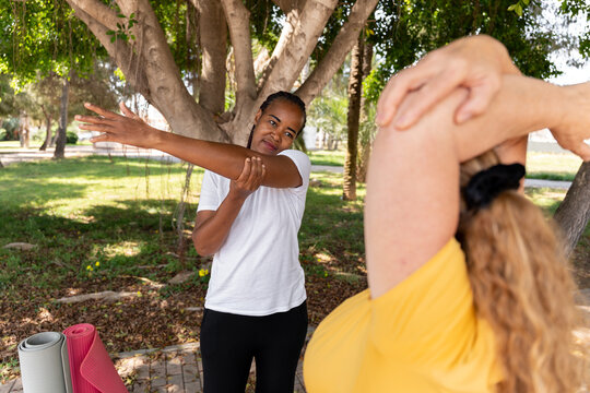Diverse women performing assisted stretching routine in outdoor setting, supporting fitness and wellness goals