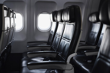 Empty airplane seats in passenger cabin. Leather chairs row inside modern aircraft interior. Bright...