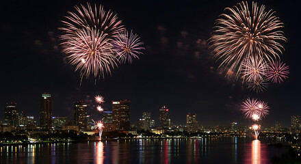 Fireworks illuminate the night sky above a city skyline, reflected in the calm water below, creating a festive.