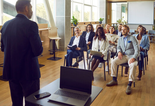 Confident business male leader rear, coach talking to diverse multiracial group of office workers, having conversation for brainstorming, discussing business strategy, ideas and team building activity - Powered by Adobe