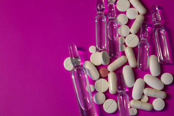 ​A close-up of various medical items, including white tablets, pills, one red tablet, and clear...