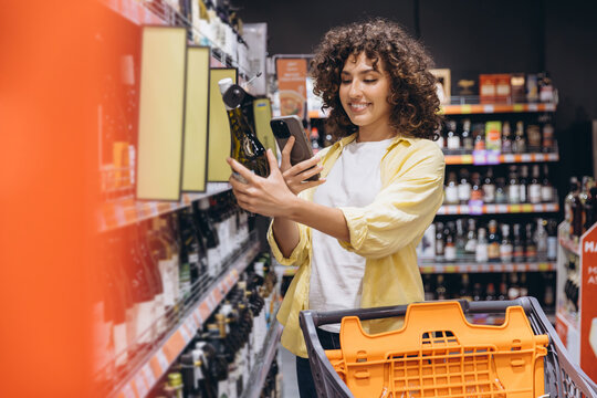 Woman scanning wine bottle with smartphone in supermarket