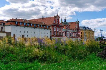 Baroque University Church in Wrocław with red and white façade, view from green meadow with flowers, historic architecture in the city center along the Oder River.