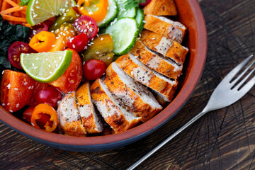Buddha bowl with baked chicken breast, chickpeas and fresh vegetables on a table in a summer cafe close up
