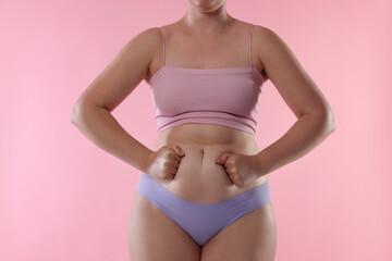 Liposuction. Woman in underwear touching her belly on pink background, closeup