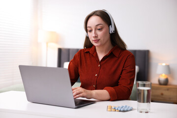 Woman in headphones having online consultation with doctor via laptop at table indoors