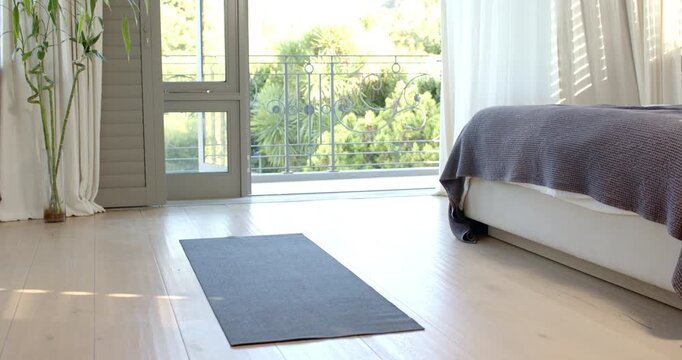 Dark grey yoga mat is lying on wooden floor in bedroom, near balcony and bamboo plant
