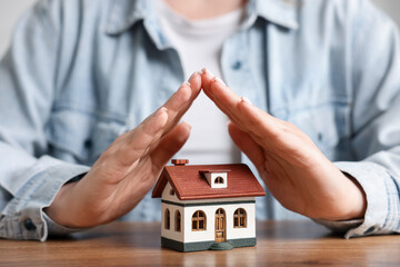Home security. Woman protecting house model at wooden table, closeup