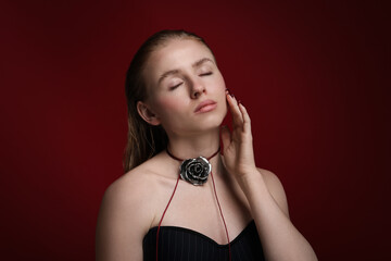 Beautiful woman in stylish necklace posing on dark red background