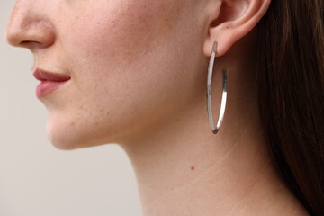 Woman wearing stylish earring on grey background, closeup