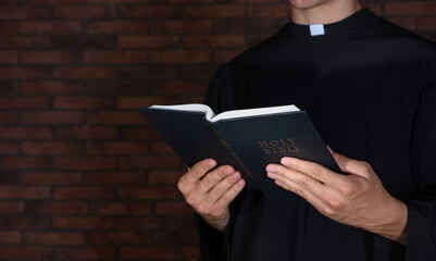Priest with Holy Bible near brick wall, closeup. Space for text