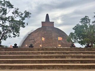 Majestic ancient brick stupa with vibrant Buddhist flags and surrounding greenery, offering a...