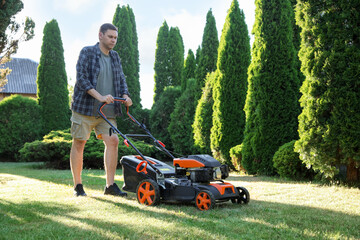 Man cutting green grass with lawn mower in garden