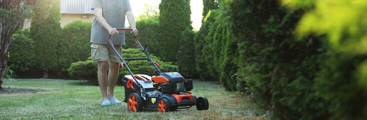 Man cutting green grass with lawn mower in garden, closeup
