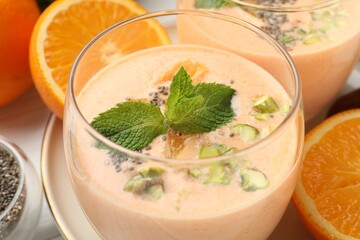 Superfood. Tasty smoothie with chia seeds, mint, pistachio and orange in glass on white table, closeup