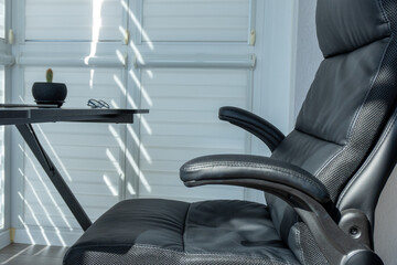 A stylish, black ergonomic chair sits beside a sleek desk adorned with a small plant and glasses,...