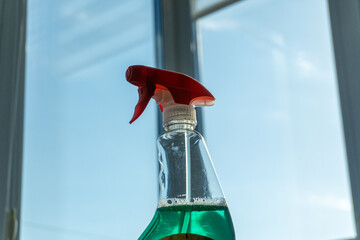 Sunlight reflects off a clear bottle of green cleaning solution topped with a red spray nozzle,...