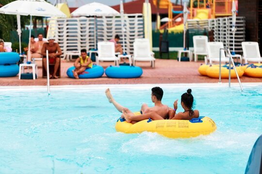Young adults relax together, floating in a yellow tube on a lazy river ride at the park, with other people sunning and enjoying the day around the blue waters - Powered by Adobe