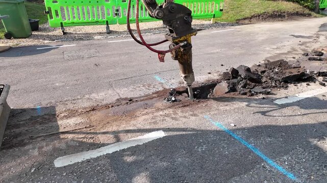 Hampshire England UK.; 07.08.2025.; Video. Hydraulic breaker attatchment breaking road surface before trench digging operation for full fibre network cable installation. UK