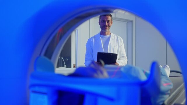 Medical worker standing confidently near MRI tunnel while female patient resting on table. Overseeing post-scan procedure inside professional medical imaging center. Patient lying on CT, PET, or MRI