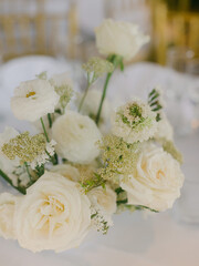 Elegant white floral centerpiece showcasing roses and greenery set on a dining table in a beautifully decorated venue