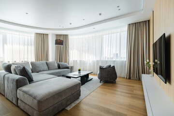 Modern living room featuring a spacious sectional sofa with large windows and stylish decor in a bright apartment setting
