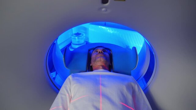 Close-up Portrait Man patient on CT MRI scanner, Bed is Moving Inside the Machine While it Scans Body and Brain. In Medical Laboratory with High-Tech Equipment. Top Down View
