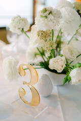 Elegant table setting featuring floral arrangement and decorative number in bright, soft-lit venue...
