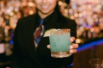 Bartender serving blue cocktail with lime garnish at a vibrant bar during evening hours