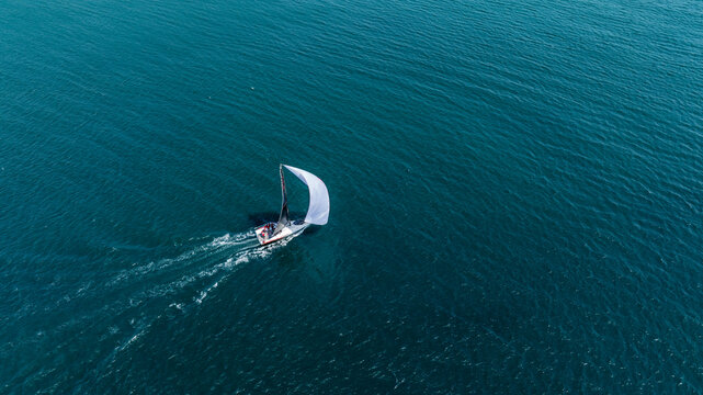Aerial View of Sailboats Racing on Open Water with Gentle Horizon. High-angle shot of multiple sailboats navigating in harmony across open blue waters under a clear sky.