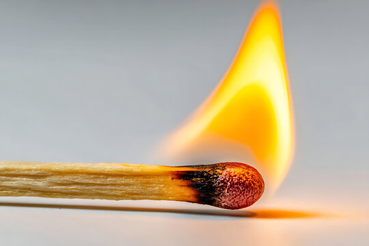 A single wooden match burning with a bright orange flame on a light gray surface fire ignition