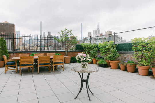 Elegant rooftop terrace with potted plants and dining area in a city skyline at dusk