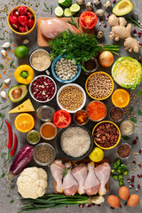 Flat lay image of a variety of healthy foods arranged Includes fresh chicken meat, colorful vegetables and fruits, leafy greens, cereals, grains, natural honey, olive oil, and spices.