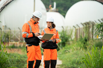 Two engineers in safety gear talking work near spherical gas storage tanks. woman is pointing...