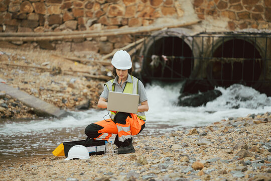 Female engineer with laptop inspecting water drainage pipes at an industrial site. Concept of environmental monitoring, infrastructure management, and technology in engineering