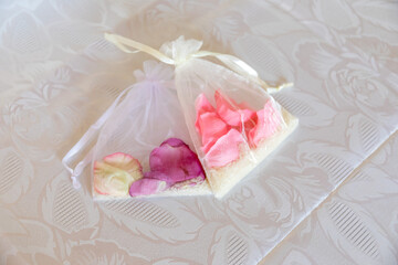 Soft organza sachets filled with vibrant rose petals lay on a finely textured tablecloth, showcasing a beautiful blend of colors that infuse warmth into any event or gathering.