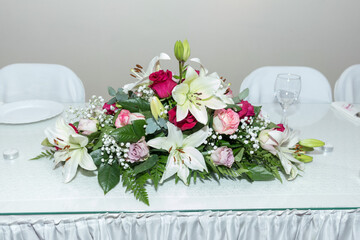A stunning display of vibrant roses and elegant lilies draws attention at a beautifully set banquet table. The arrangement, bursting with color, enhances the festive atmosphere of the event.