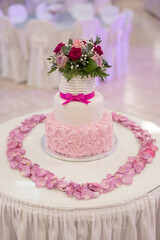 A stunning two-tier cake with pink rosette icing sits on a table adorned with delicate rose petals. Fresh flowers top the cake, creating a festive atmosphere for a special occasion.
