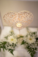 A beautifully crafted heart sculpture adorned with intricate designs glows softly, surrounded by fresh white flowers, creating a serene atmosphere during a wedding ceremony.