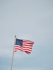 Obraz premium American flag waving on a flagpole against a clear blue sky on a sunny day