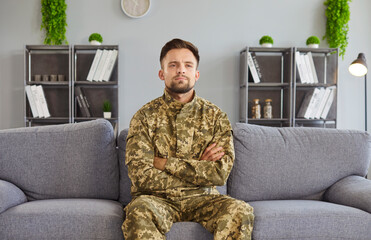 Man wearing military camouflage, arms being crossed, serious, soldier suffers with war memories, flashbacks, negative thoughts after traumatic event, alone at home in anxiety or irritability