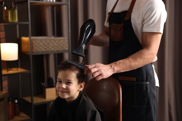 Professional barber blow drying boy's hair in barbershop, closeup