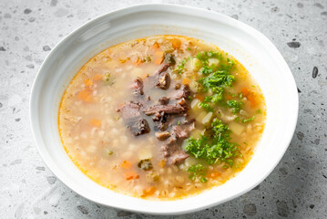 Homemade beef barley soup with vegetables and fresh parsley in a white bowl on a speckled...