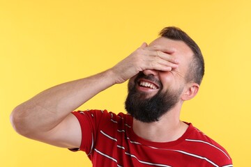 Fototapeta premium Man covering eyes and laughing on yellow background