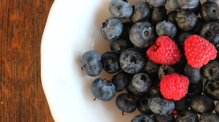 Freshly picked raspberries and blueberries in clean bowl on a rough wooden table
