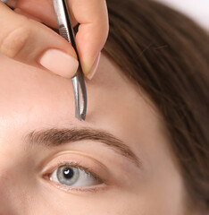 Cosmetologist plucking young woman's eyebrow with tweezers, closeup