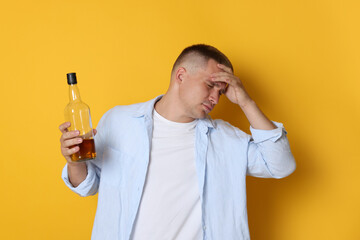 Man with bottle of whiskey suffering from hangover on orange background