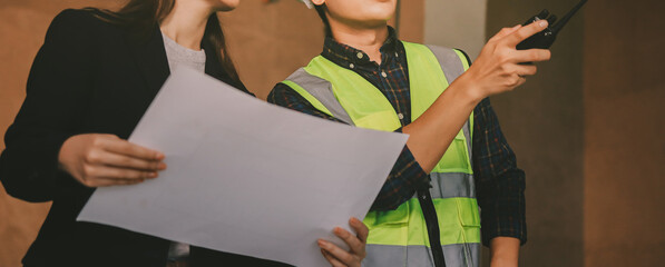 Construction manager and engineer dressed in orange work vests and hard helmets explore...