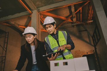 Construction manager and engineer dressed in orange work vests and hard helmets explore...