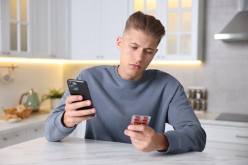 Sick man with pills having online consultation with doctor via smartphone at white marble table in...